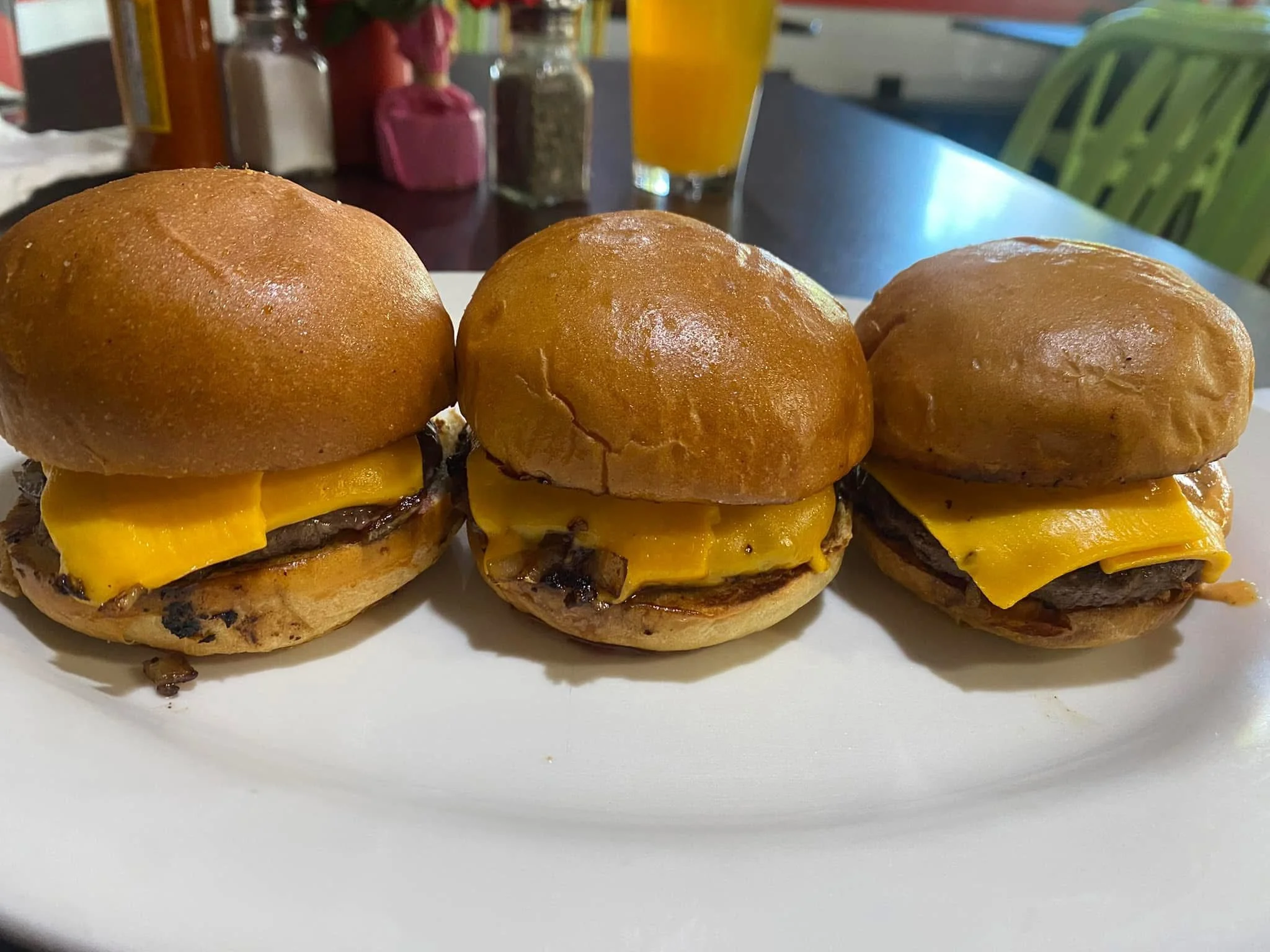 Three cheeseburgers with beef patties and melted cheddar cheese on a white plate