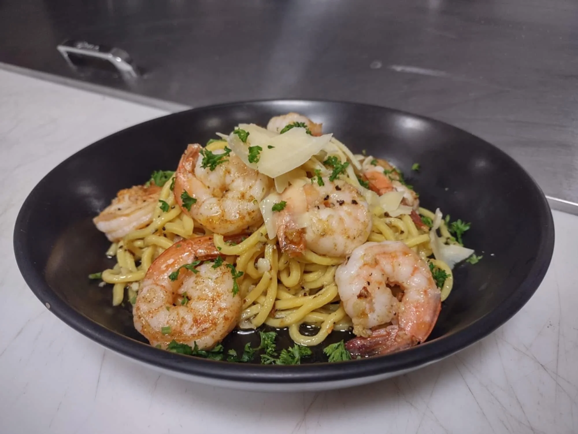 Shrimp and pasta dish garnished with fresh herbs on a black plate
