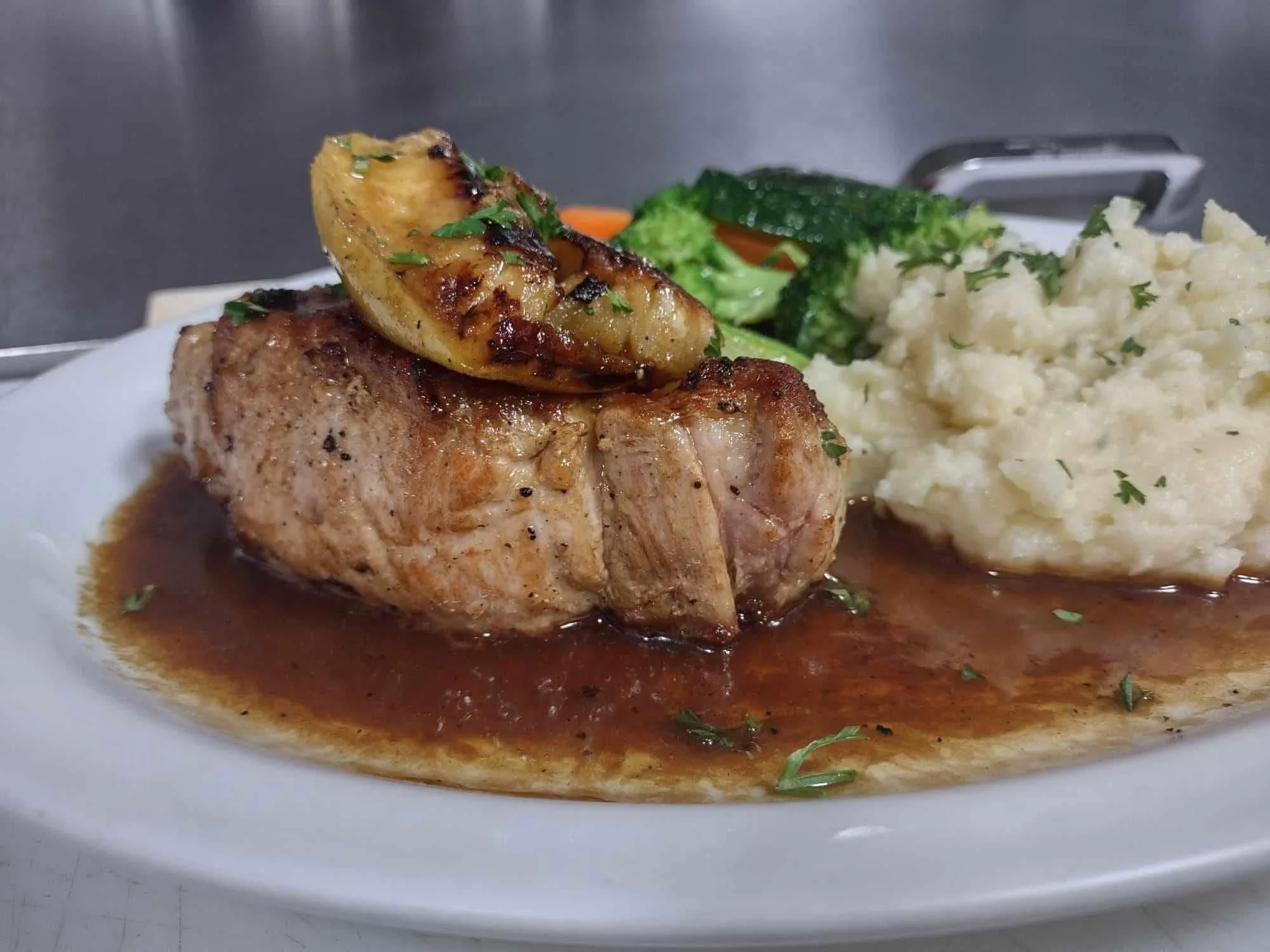 A plate of cooked chicken breast topped with grilled lemon, served with mashed potatoes and steamed broccoli.