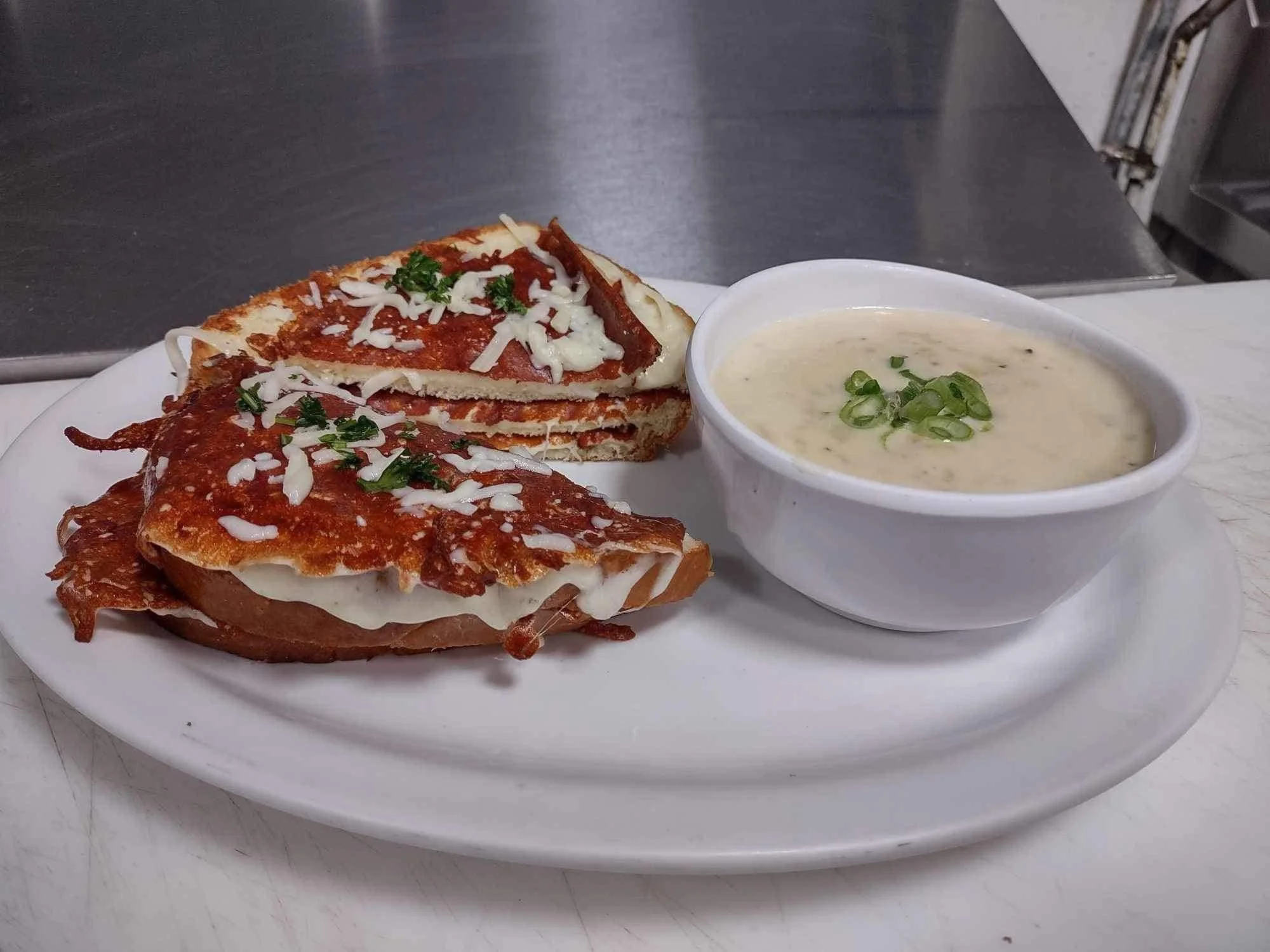 Plate with eggplant Parmesan, slices of lasagna, and a bowl of cream soup garnished with chopped green onions.