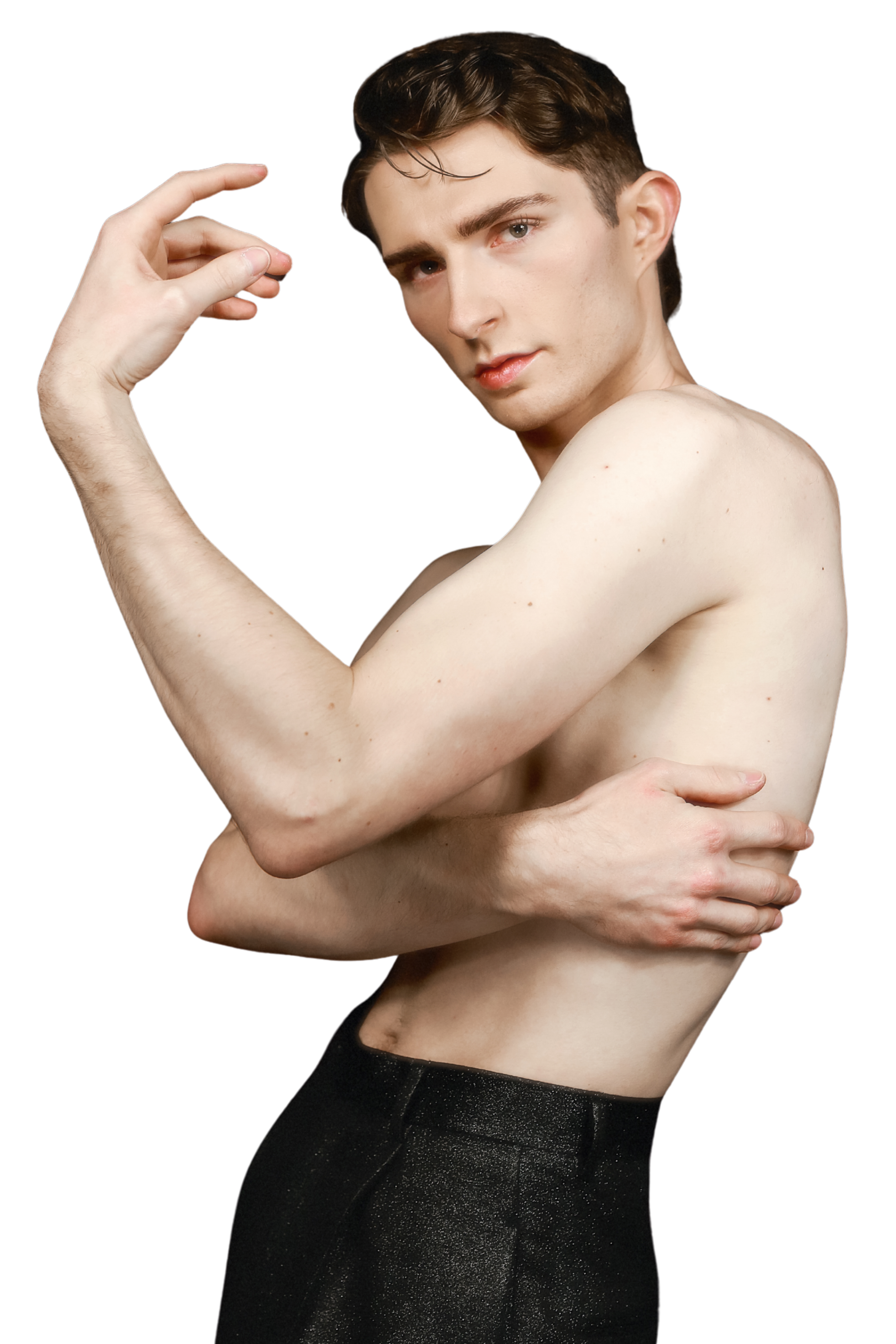 A shirtless young man with short brown hair and fair skin posing against a black background. He is making a peace sign with his right hand near his head and has his left hand on his waist, wearing black glittery pants.