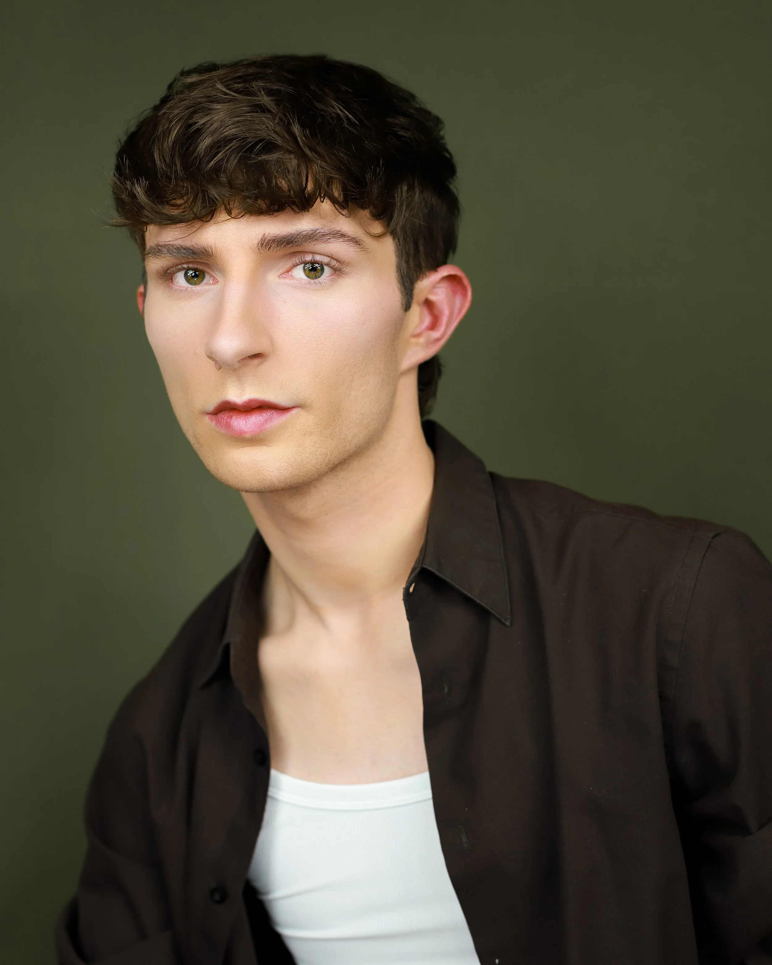 Close-up of a young man with brown hair, green eyes, wearing a black shirt, white undershirt, against a green background.