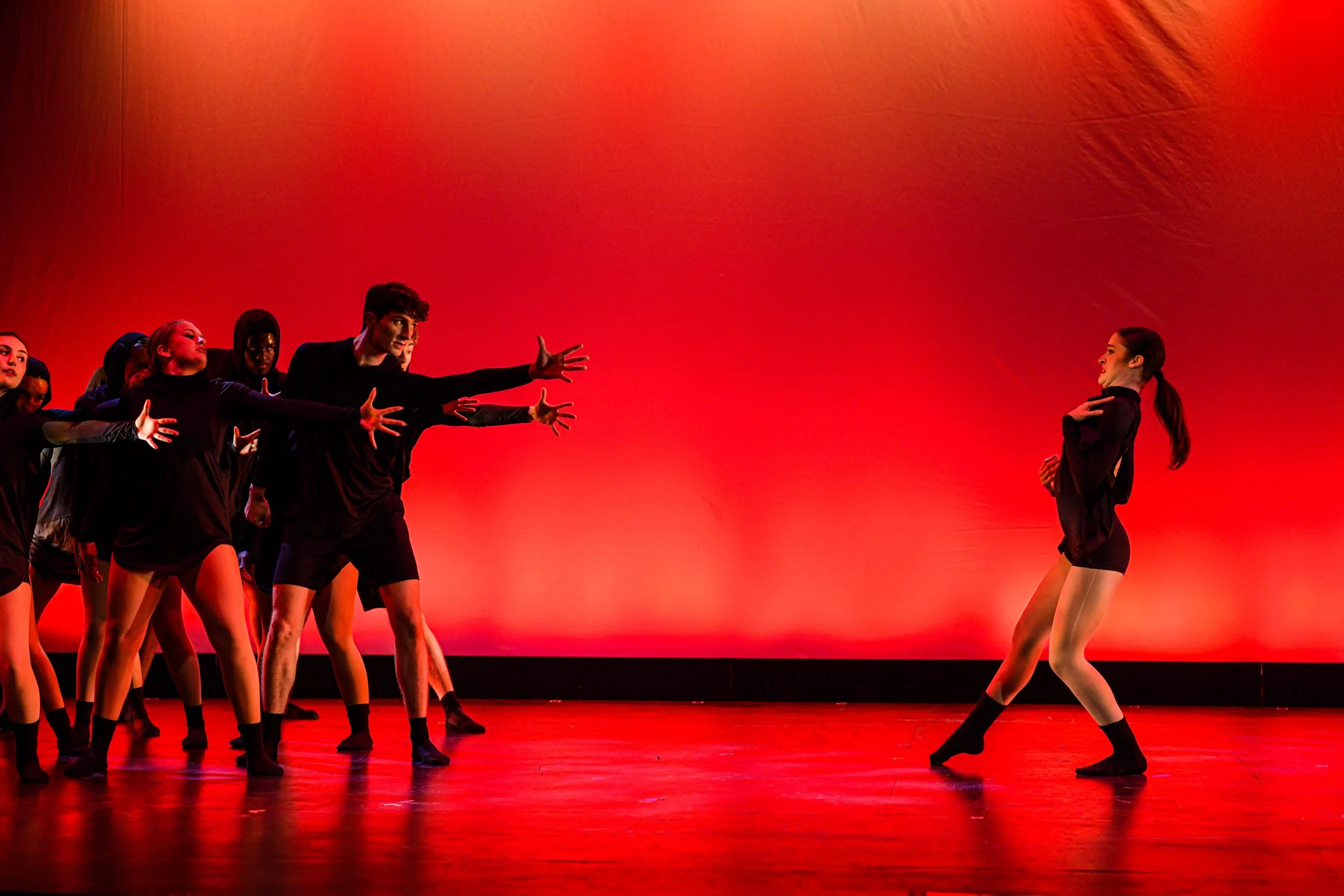 Dancer on stage performing in front of a group of dancers against a red background.