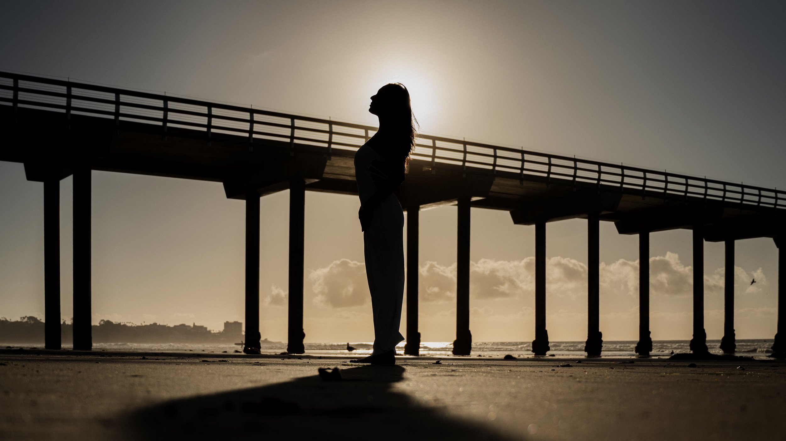 Silhouette of a person standing on a beach near a pier during sunset at Scripps Memorial Pier in La Jolla, CA. 