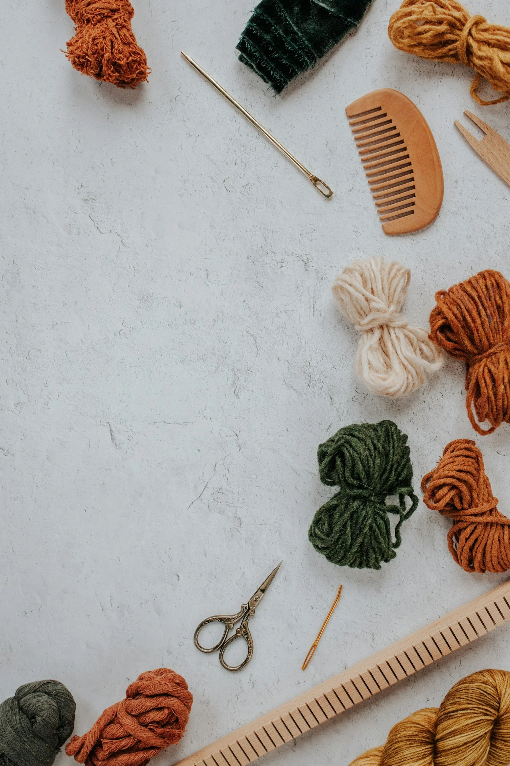 Various skeins of yarn in different colors, knitting tools, and accessories scattered on a light textured surface.