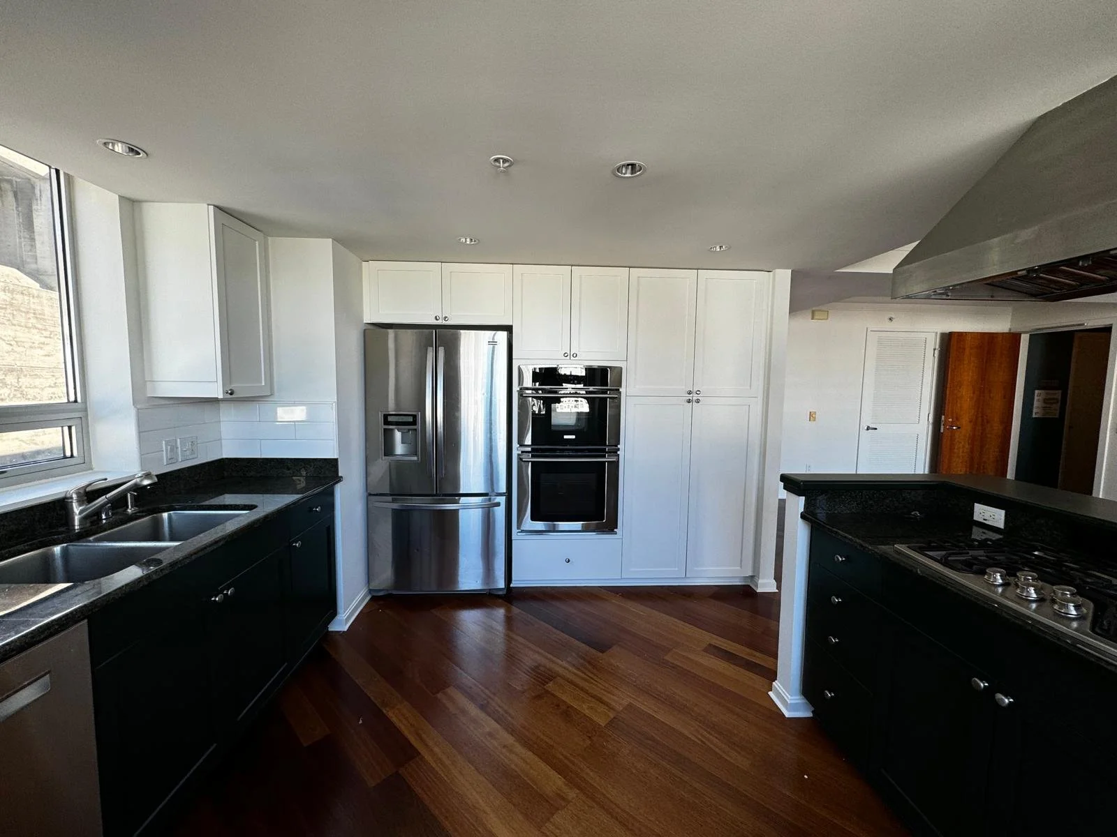 Modern kitchen with black countertops, white cabinets, stainless steel refrigerator, and wooden flooring.