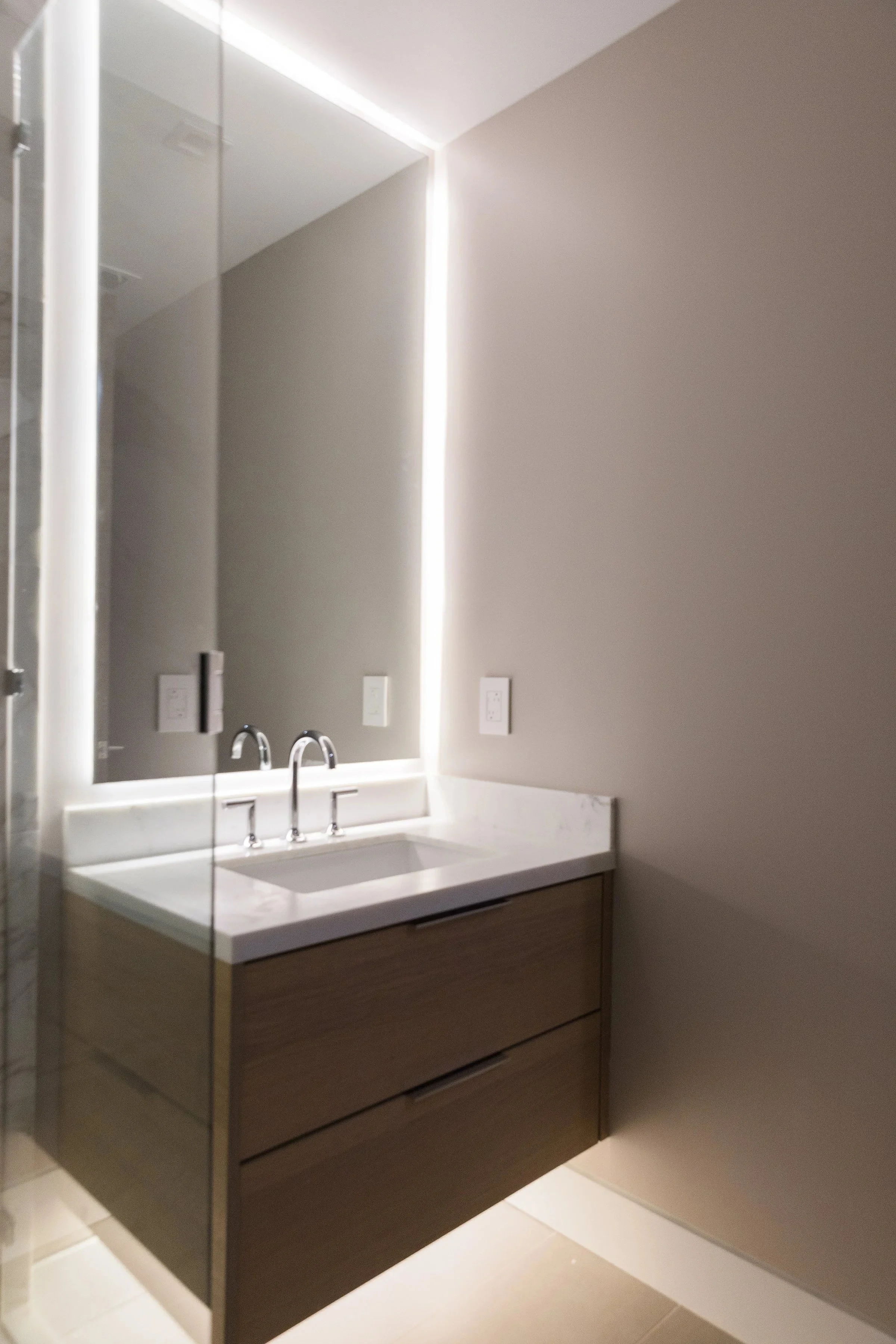 Modern bathroom vanity with a white marble countertop, a rectangular sink, and a large mirror with LED lighting. The vanity has two wooden drawers beneath the sink.