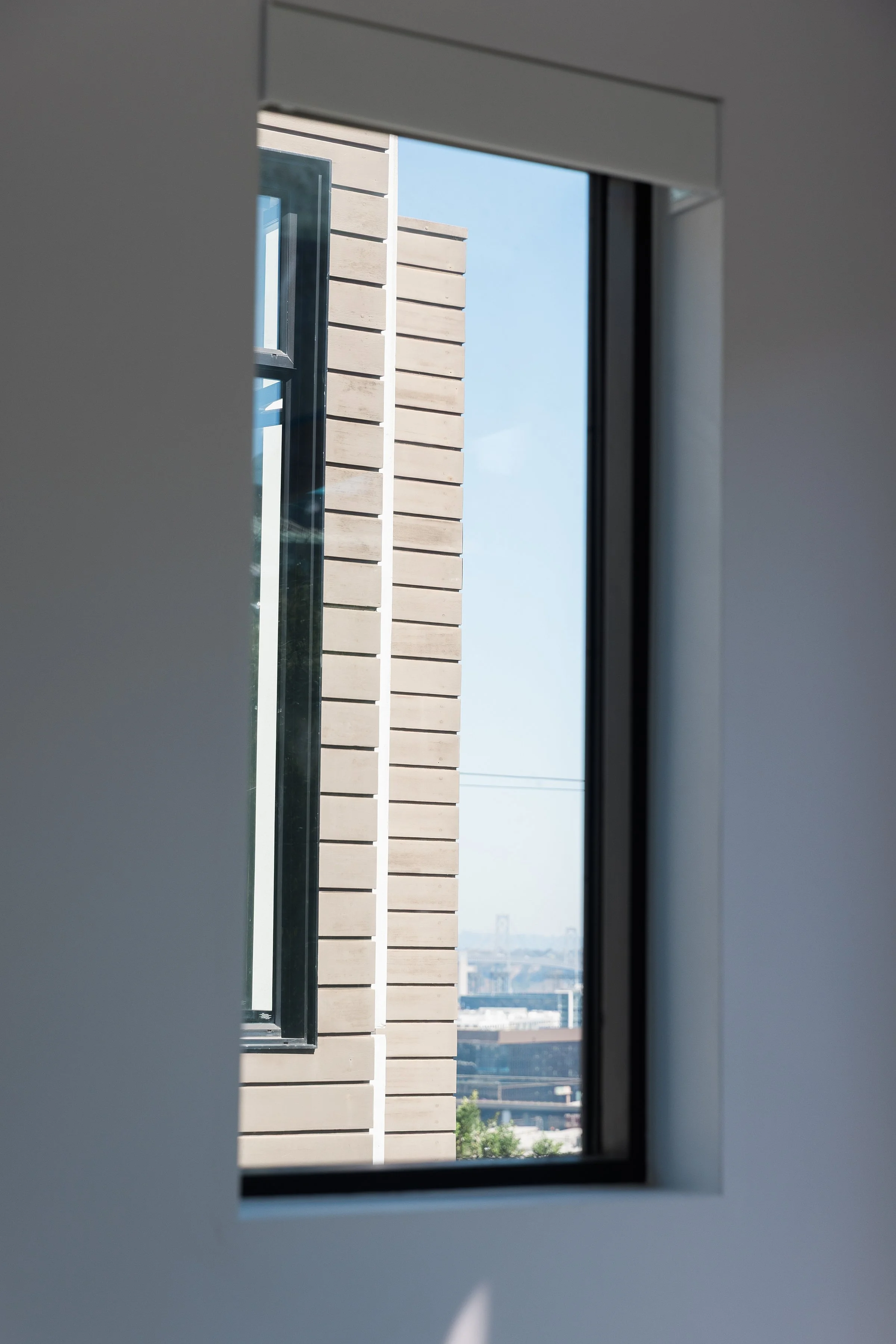 View of a city skyline through an open window with a beige brick building in the foreground.