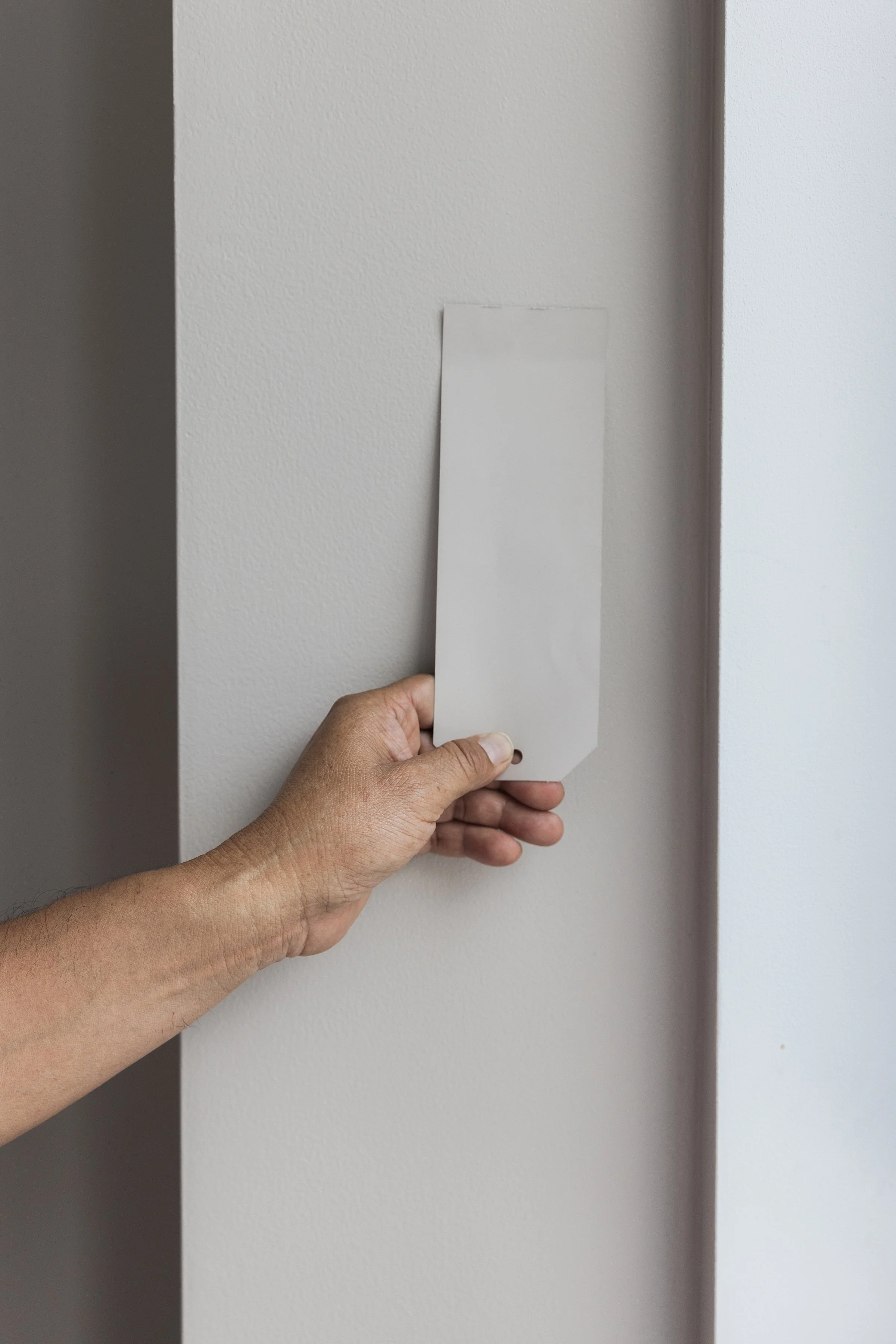 A person holding a white blank name tag or ID badge in front of a white wall.