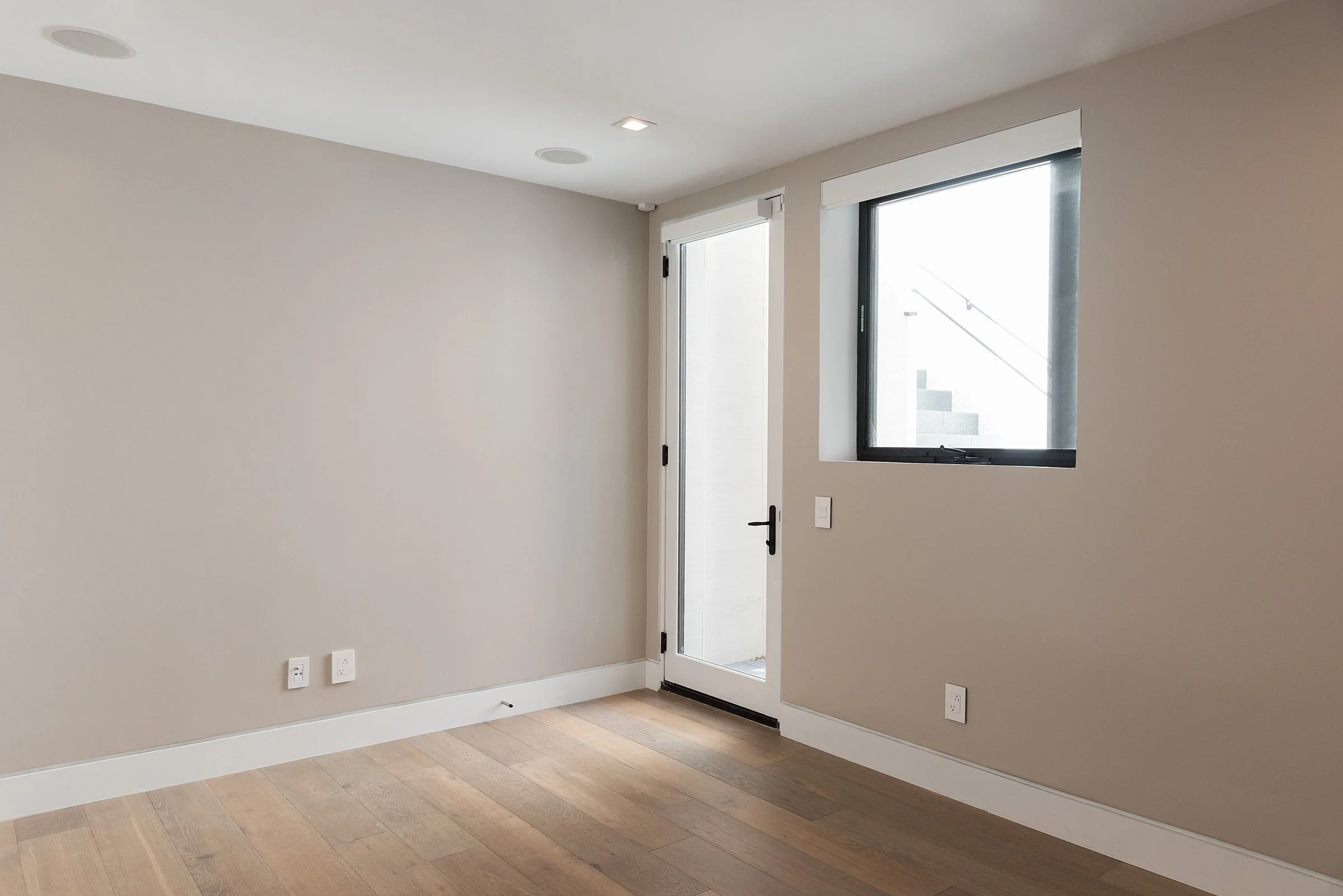 Empty room with hardwood floors, a window, a door, and multiple electrical outlets.