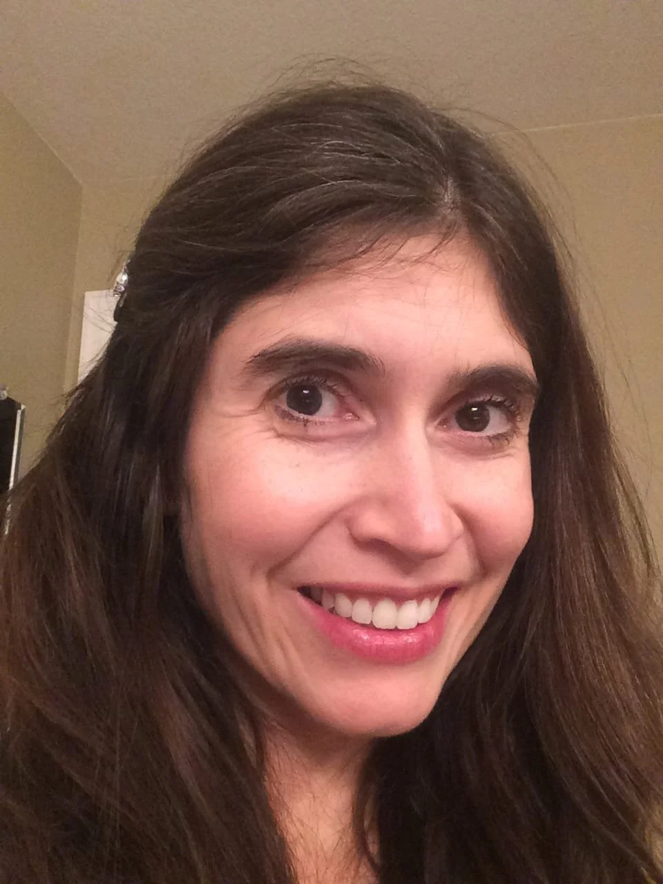 Close-up of a smiling woman with long brown hair and light skin, indoors.