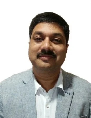 A man with dark hair and a mustache, wearing a light gray blazer and white shirt, smiling at the camera.