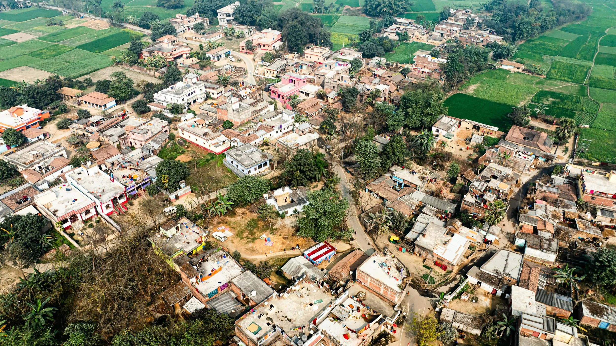 Aerial view of a rural village with houses, roads, and green fields surrounding the settlement.