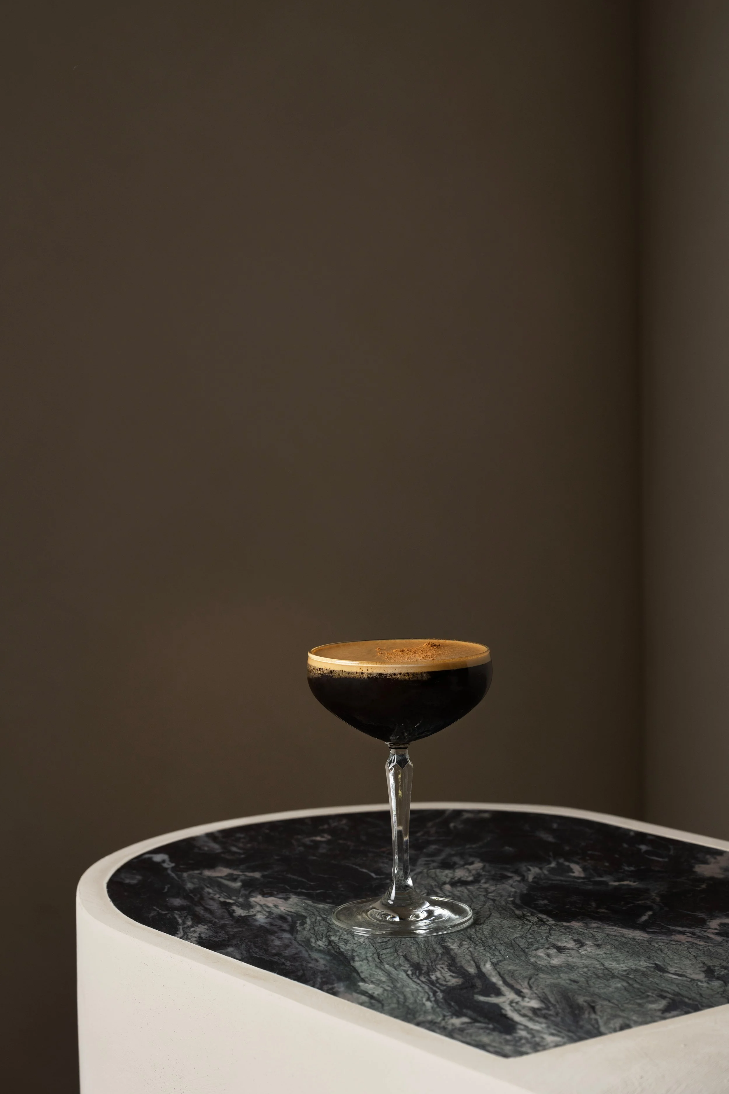 A glass of dark beverage on a black and white marble surface with a gray background.