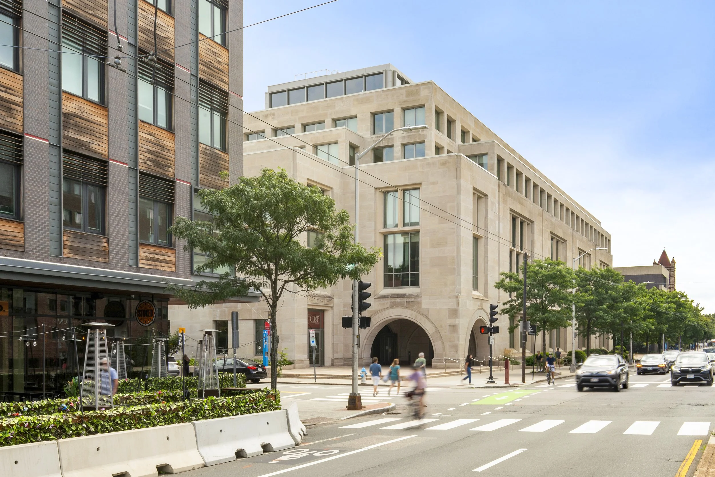 City street intersection with modern buildings, people crossing, and cars driving during daytime.