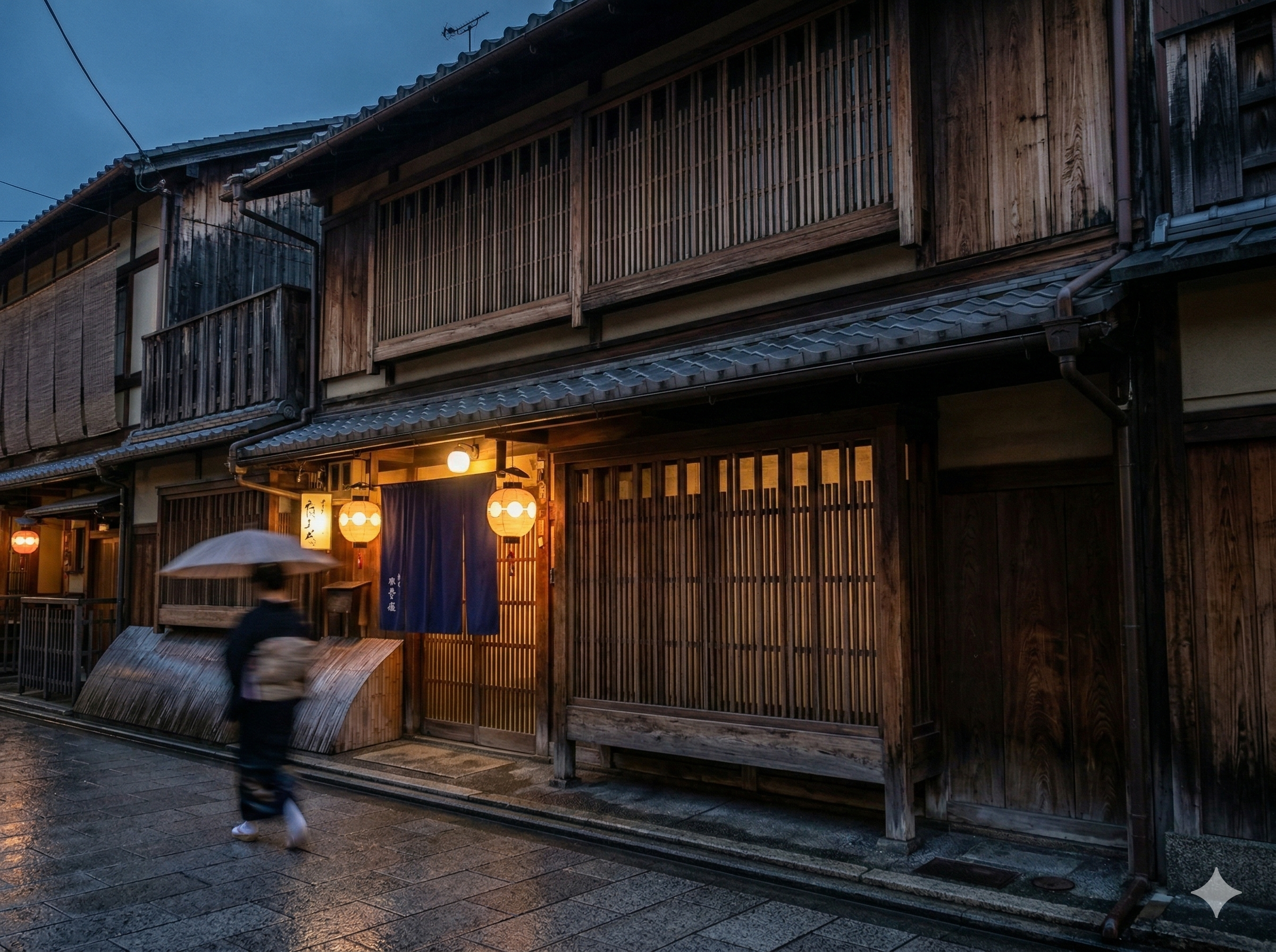A traditional Japanese building with wooden siding and paper lanterns hanging outside, illuminated during dusk. A person with an umbrella walks by on the wet street.
