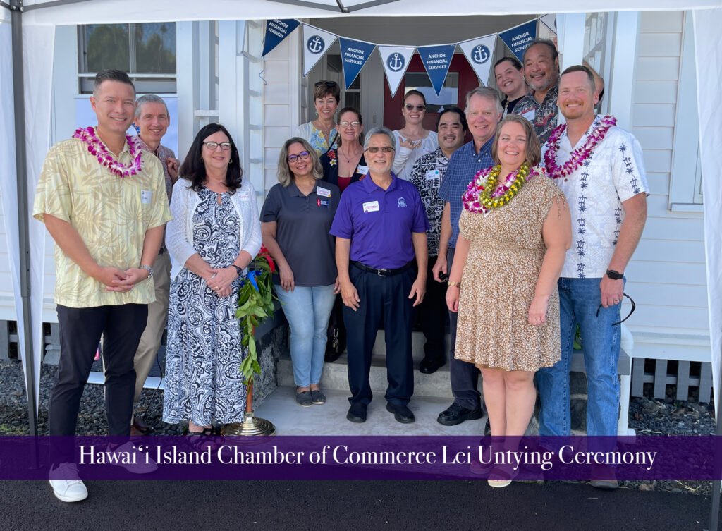 A group of people gathered outside a building for Hawaii Island Chamber of Commerce Lei Untying Ceremony, with some wearing leis and smiling for the photo.