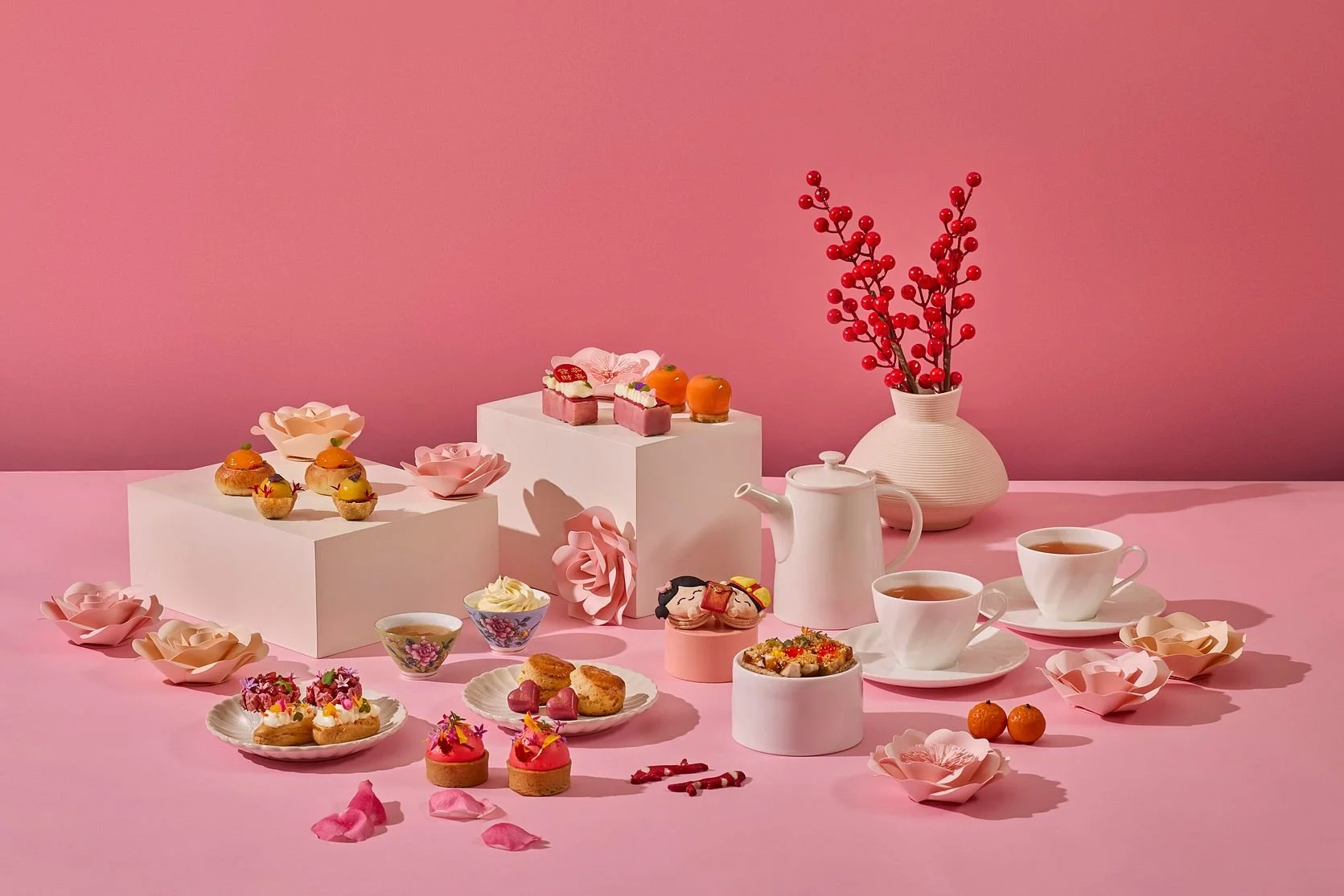 Pink-themed tea party setup with assorted desserts, tea cups, teapot, and decorative flowers and branches.