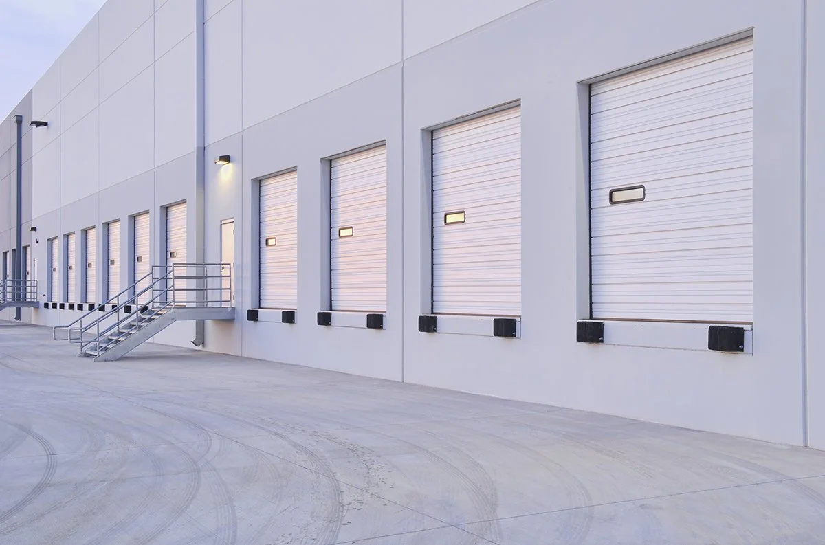 Industrial warehouse loading dock with multiple roll-up doors and metal access stairs