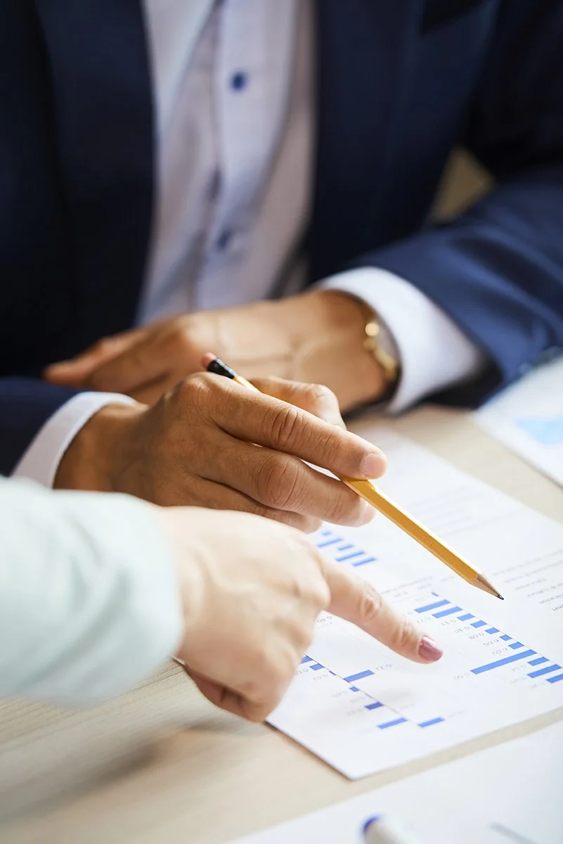 Business professionals reviewing a financial chart, with one pointing and another holding a pencil.