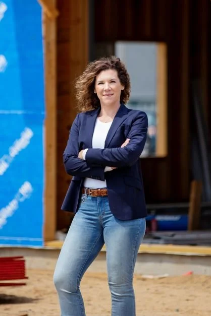 Confident woman in a navy blazer and jeans standing with arms crossed at a construction site