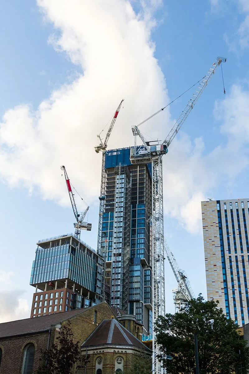 High-rise construction site with multiple tower cranes beside a historic church under a blue sky