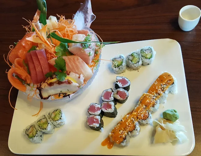 Assorted sushi rolls, sashimi, and a seafood salad with sliced fish, shrimp, and garnishes on a tray.