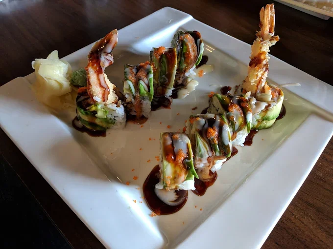 Sushi rolls with shrimp tempura, avocado, cucumber, and eel sauce on a white square plate, with ginger and wasabi on the side.