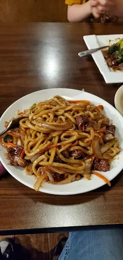 Plate of stir-fried noodles with vegetables and meat on a wooden table.