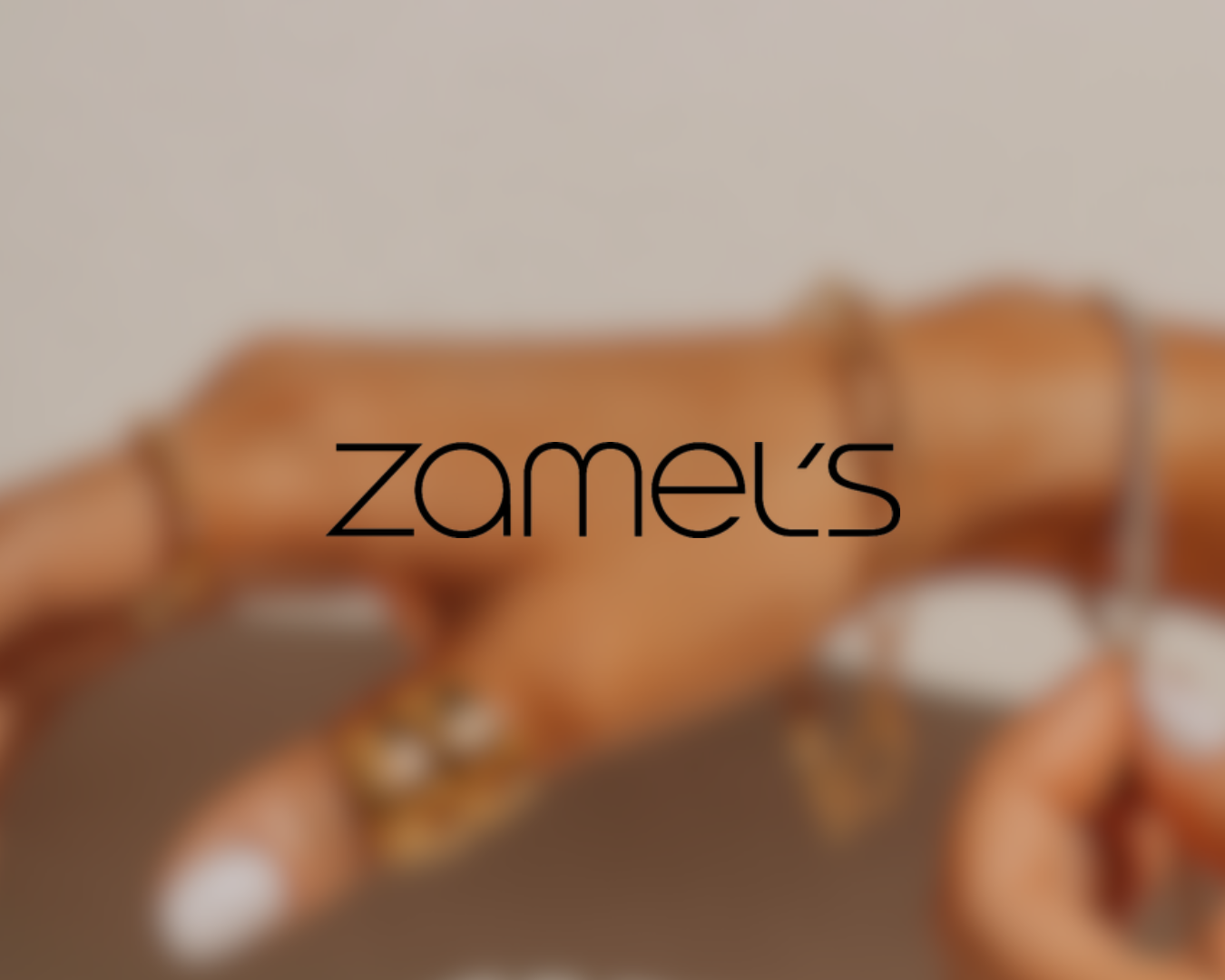 Blurred image of a hand with white nail polish holding a banded jewelry piece, with the word 'zamek's' overlayed in black text.