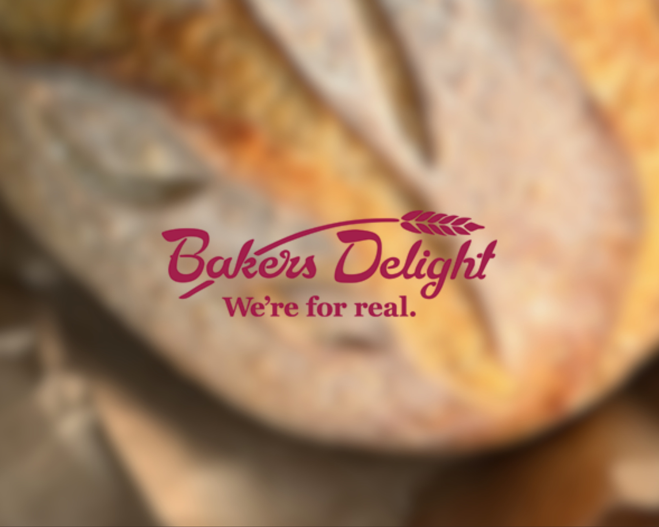 Blurred image of baked goods with a bakery logo that says 'Bakers Delight' and the slogan 'We're for real'.