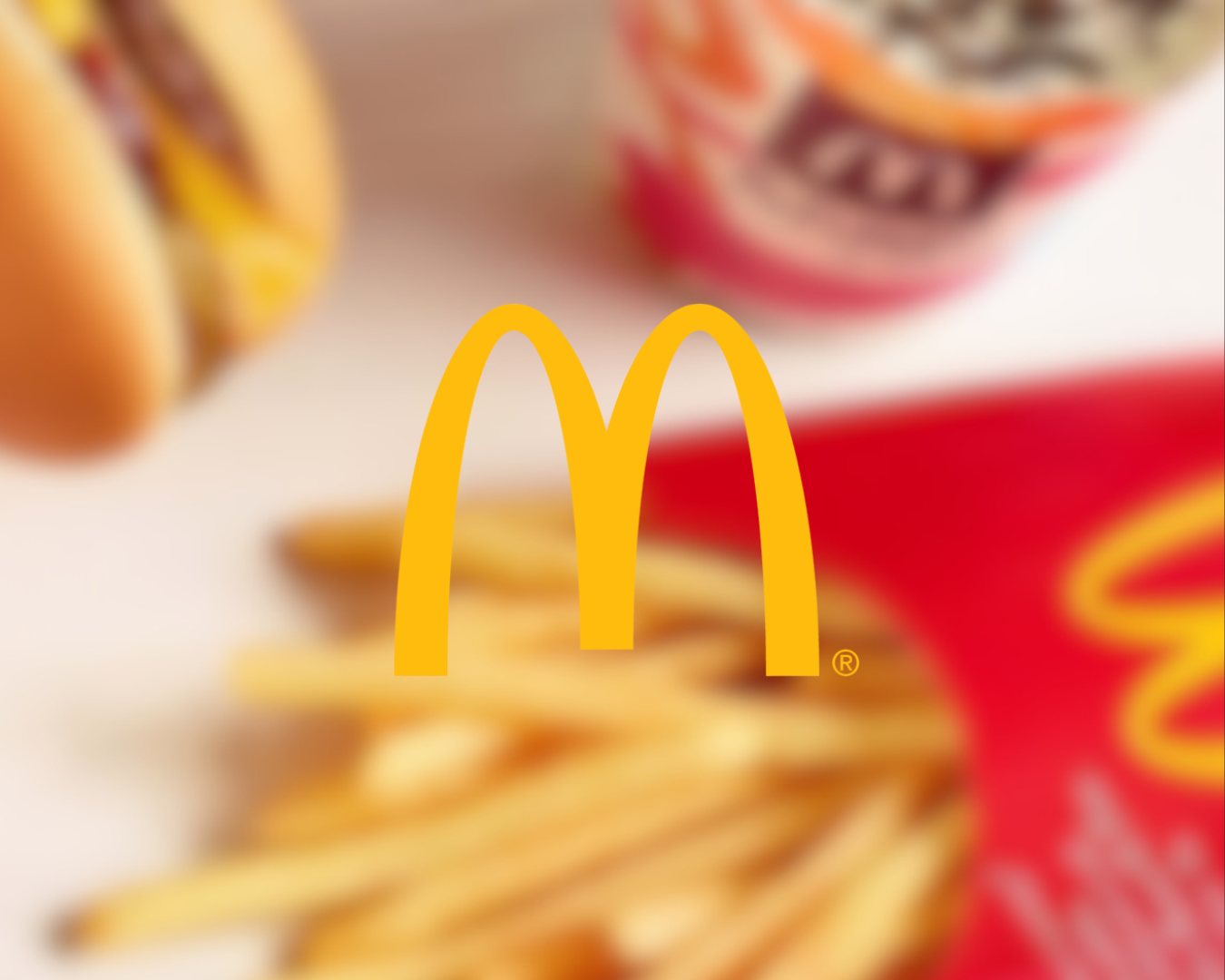 Close-up of McDonald's French fries, a burger, and a soft drink with the McDonald's logo in the foreground.