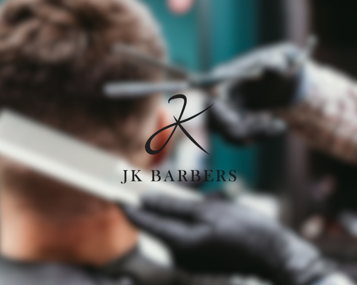 Blurred image of a person receiving a haircut at JK Barbers with scissors in hand.