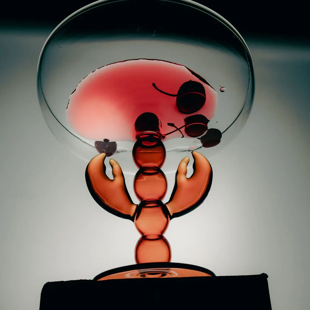 A glass sculpture of a scorpion holding a glass of red wine, with the wine visible through the transparent body of the sculpture.