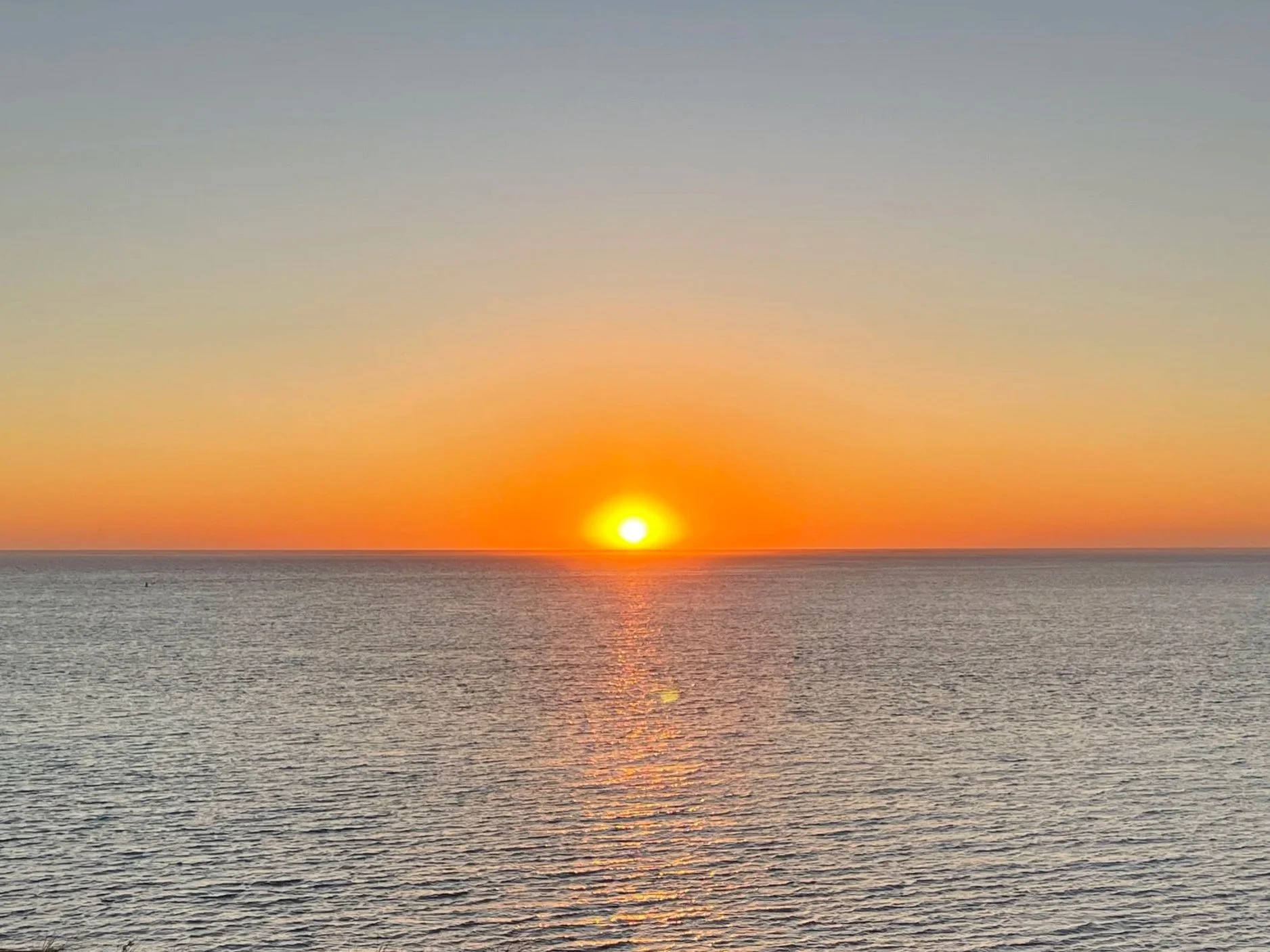 Sunset over ocean with a clear sky and colorful horizon.