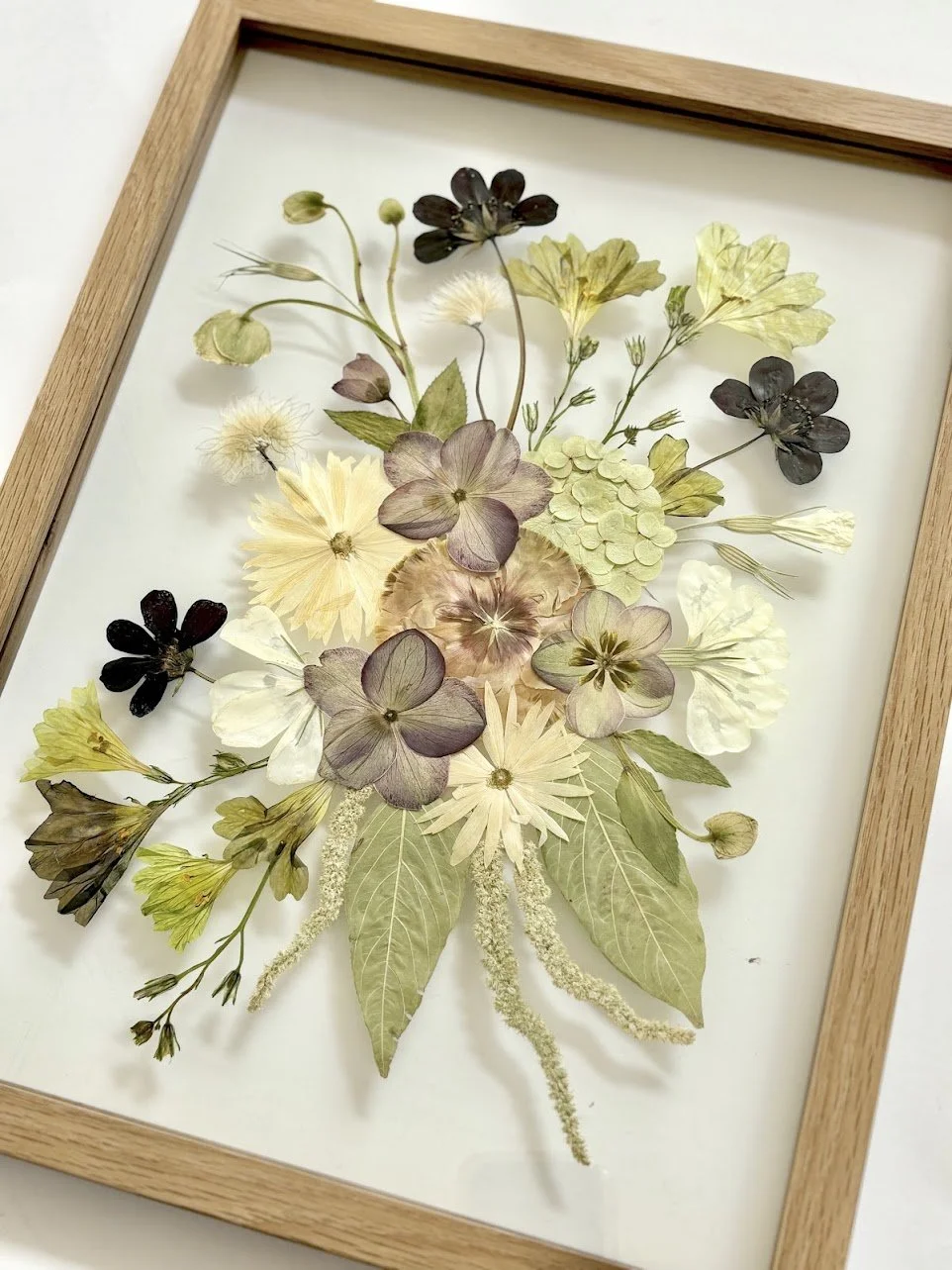 Pressed dried flowers and leaves arranged in a floral display inside a wooden frame.