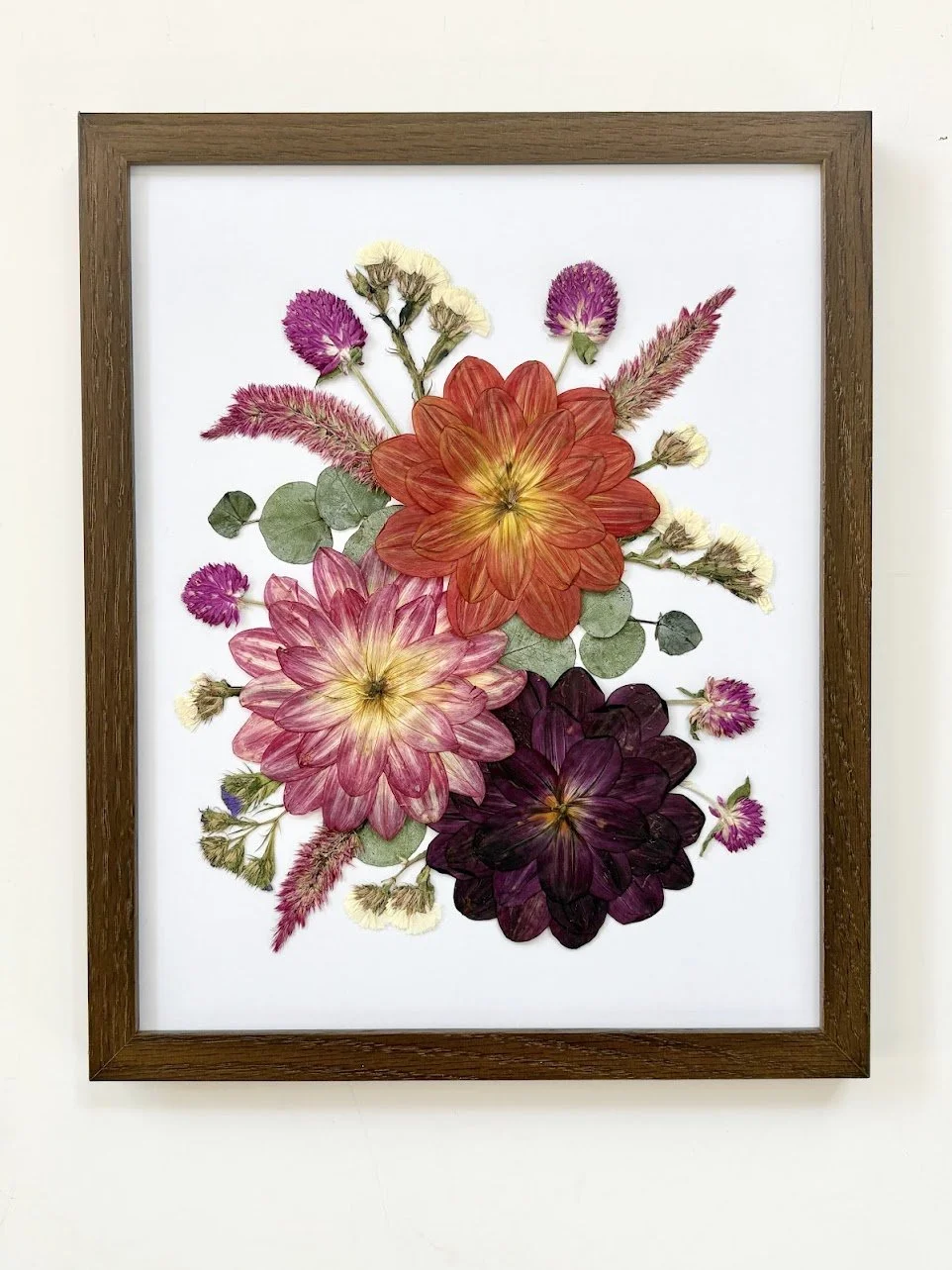Framed artwork of pressed and dried flowers arranged in a floral pattern on white background.