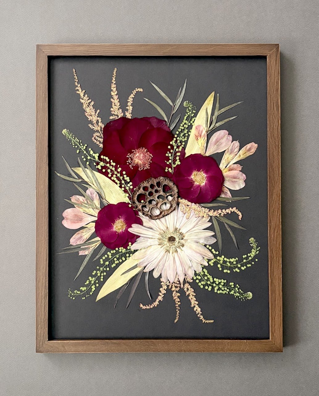 Framed botanical artwork featuring deep red and pink flowers, white blooms, green foliage, and a dried seed pod.