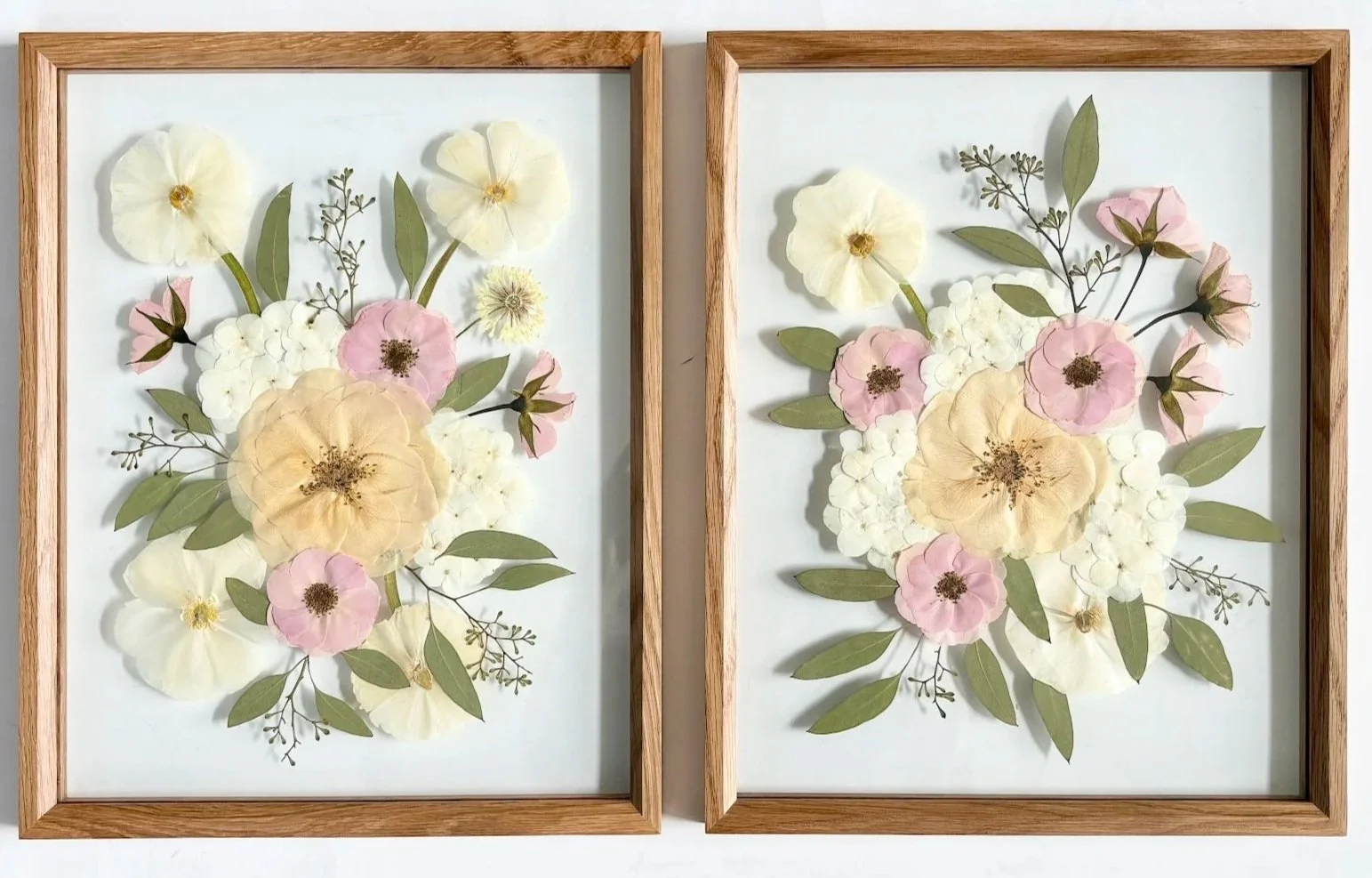 Two framed pressed flower art pieces with pink, white, and cream flowers and green leaves on white backgrounds.