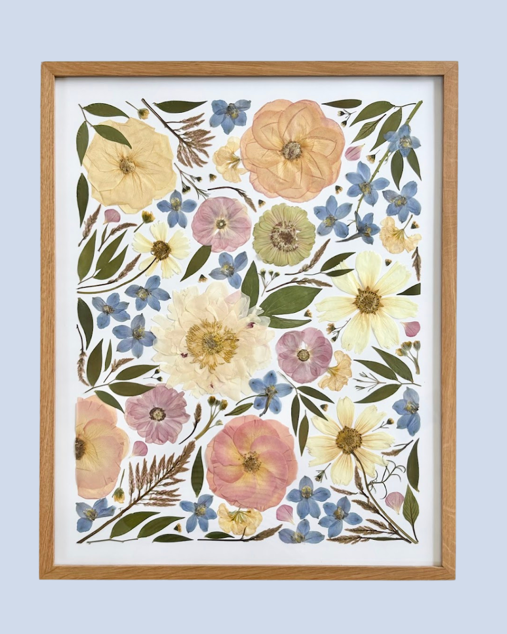 A framed botanical print featuring dried pressed flowers and foliage, including large cream, pink, and yellow flowers, smaller blue flowers, and green leaves against a white background.