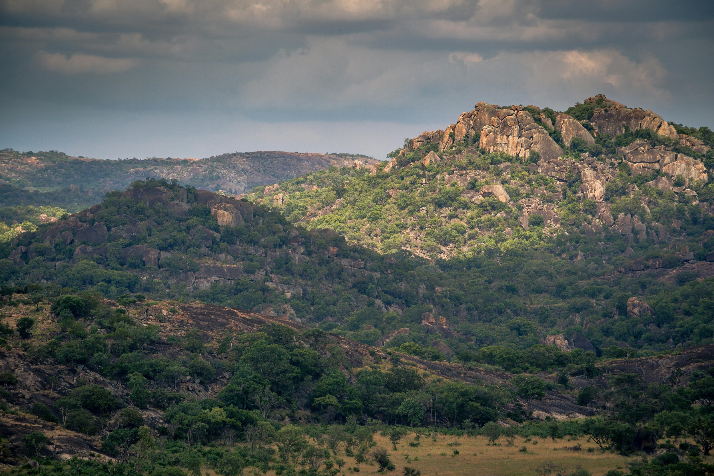 Landscape of rocky hills covered with green trees and shrubs under a cloudy sky.