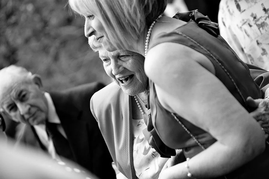 Three elderly women smiling and laughing together, sharing a joyful moment at a social gathering.