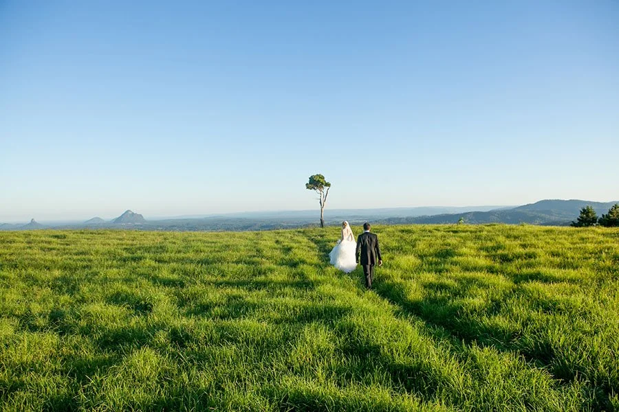 A bride and groom walking through a lush green field at One Tree Hill, Maleny, Sunshine Coast 