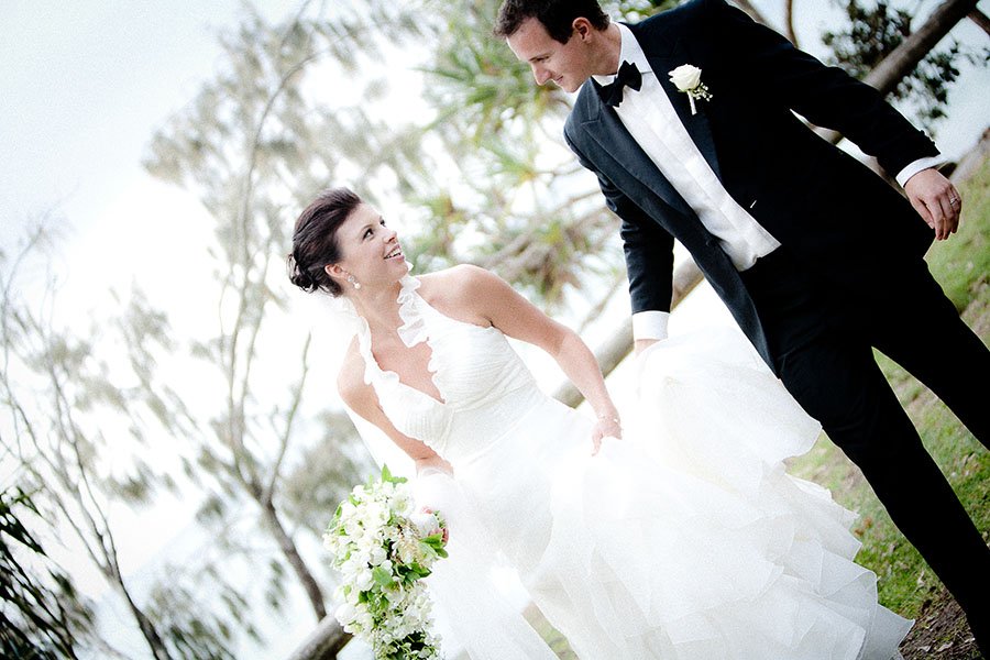 Bride and groom smiling at each other outdoors on their wedding day, with trees in the background.