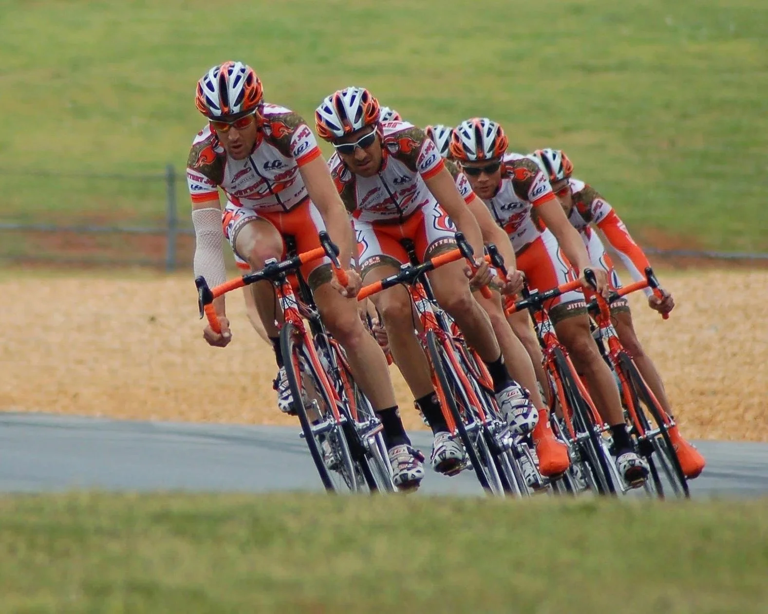 Fünf Radrennfahrer in roten und weißen Trikots und Helmen bei einem Rennen auf einer Rennbahn.
