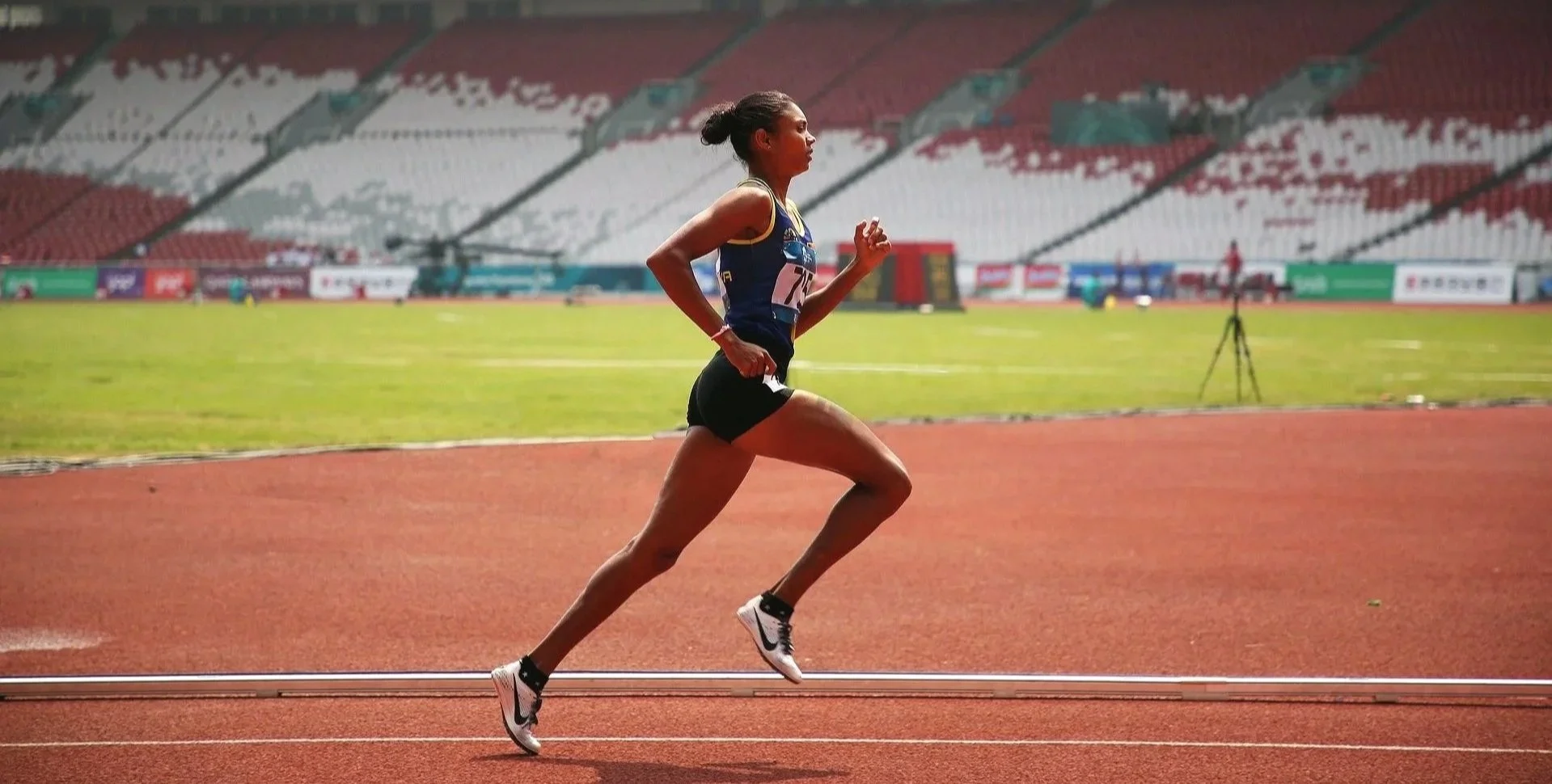 Leichtathletin läuft auf einer Wettkampfbahn im leeren Stadion.