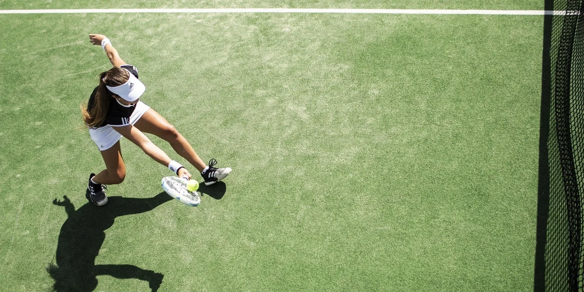 Eine Tennisspielerin beim Aufschlag auf einem grünen Tennisplatz, die Schatten wirft.