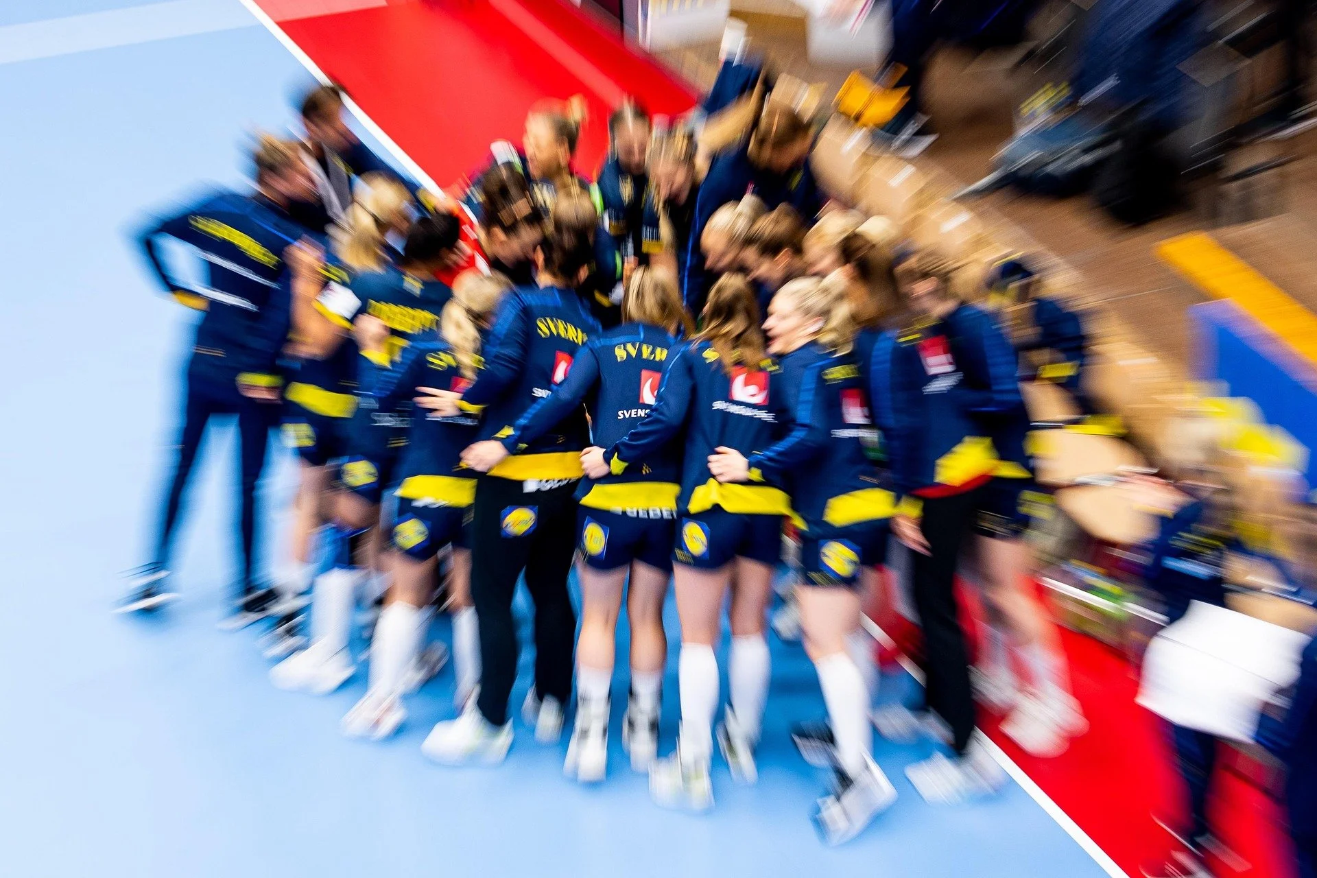 Team von Sportlerinnen und Sportlern in blauen und gelben Trikots, die sich umarmen und sich auf einer Turnhalle befinden.