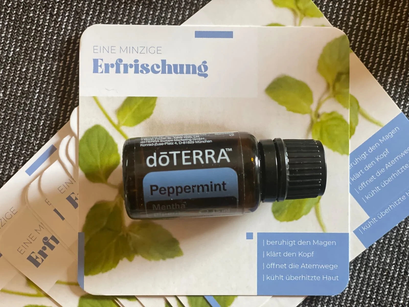 Kleine Flasche doTERRA Pfefferminzöl auf einer Werbeunterlage mit grünen Minzblättern und blauer Beschriftung, Hinweis auf beruhigende, klärende Wirkung auf Magen, Kopf, Atemwege und Haut.