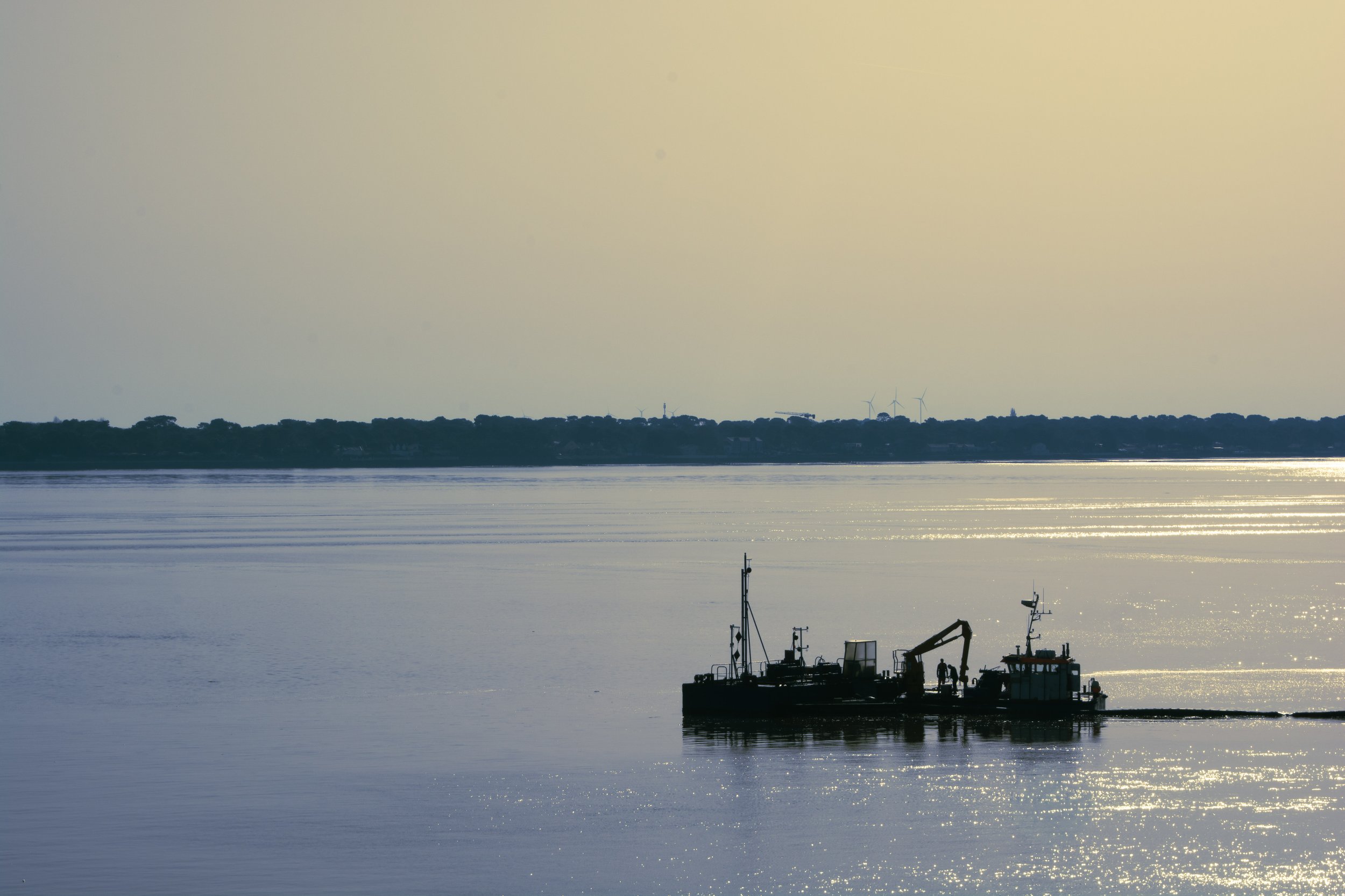 A boat on calm water during sunset with wind turbines visible in the distance on the horizon.